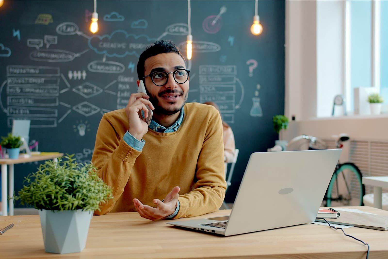 Young man laughing on a phone call at his laptop in a start-up office