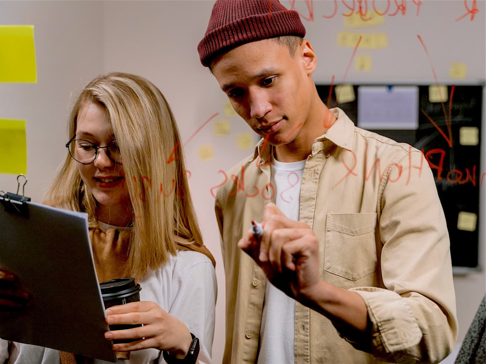 Two young colleagues collecting ideas on a glass wall with sticky notes
